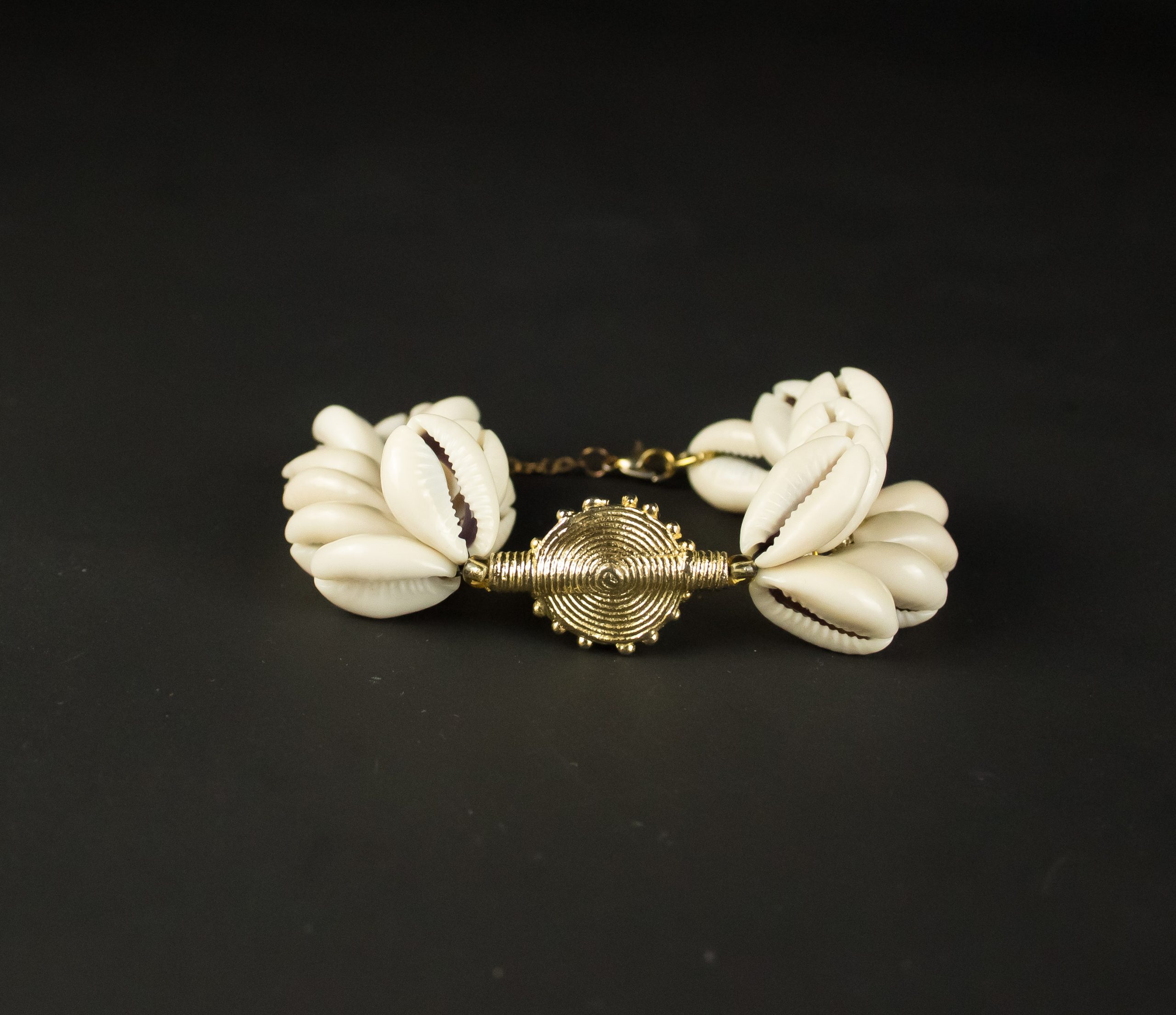 Bracelet Jojo Création Cascade de Cauris en métal doré avec plusieurs coquillages cauris, présenté sur fond sombre